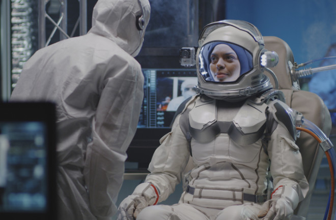 Medium shot of a female astronaut testing spacesuit camera and listening to instructions during pre-flight preparation