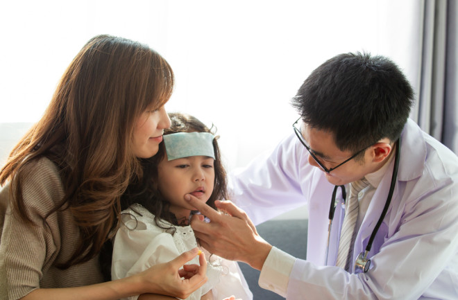 Mother with sick young daughter in hospital. Doctor treating child with cool fever gel on forehead for rsv