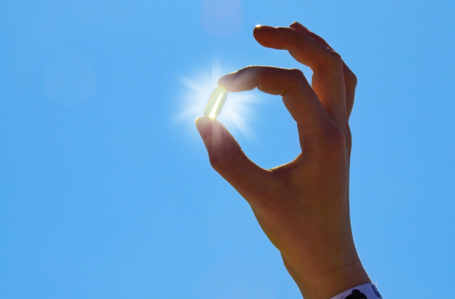 Young Woman is holding Vitamin D Capsule. Sun and blue Sky.