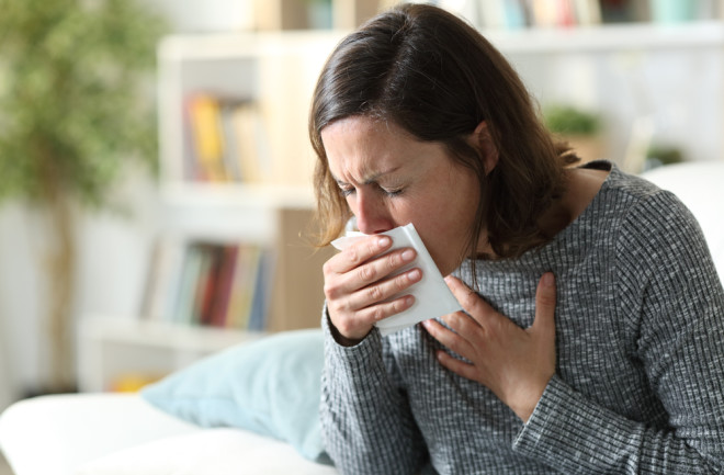 woman coughing at home into a tissue phlegm mucus illness - shutterstock