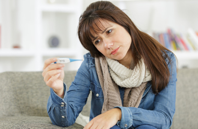 Woman taking her temperature, fever - Shutterstock