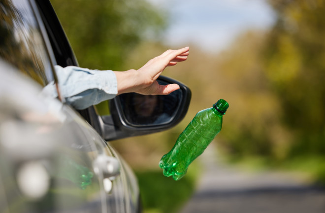 Close Up Of Driver In Car Dropping Trash Out Of Window On Country Road