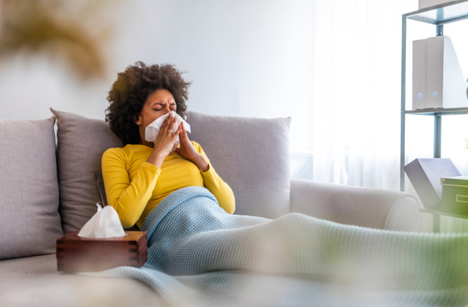 Yound sick woman sweating and sneezing at home in tissue from flu. Sick woman with runny nose.