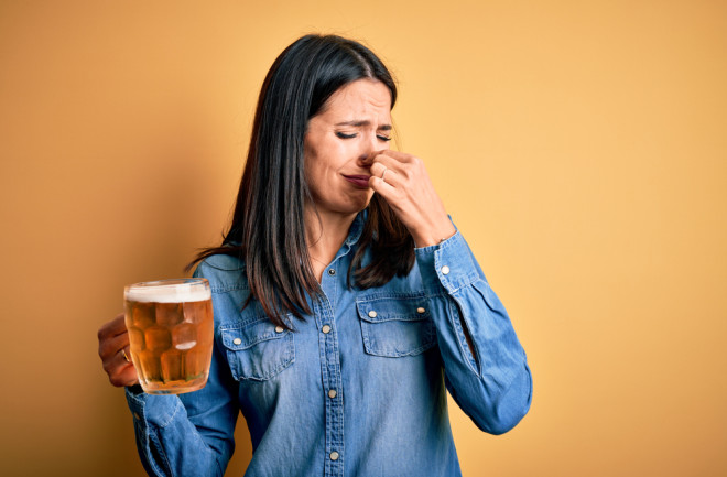 woman holding her nose in one hand a beer in the other hand, having a bad reaction to alcohol